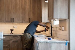 A man works on a kitchen sink, highlighting his role in fixture refinishing for both bathrooms and kitchens.