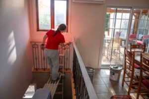 A woman applying paint to the stairs in a home, highlighting her expertise in fixture refinishing for bathrooms and kitchens. 