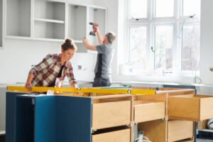 A man and woman collaborating on assembling a kitchen cabinet in a well-lit workspace, guided by expert kitchen remodelers Plainfield IL.
