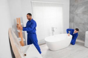 Two women in blue work clothes installing fixtures during a bathroom renovation project led by a professional bath remodel contractor.