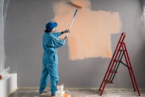 A man in a blue suit is painting a wall with a roller, demonstrating a professional approach to wall painting.