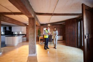 Two individuals standing in a spacious room with wooden floors, showcasing a home remodeling project.