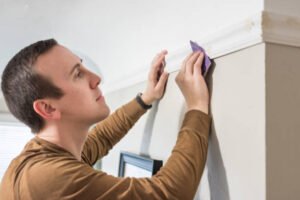 A man cleans the Crown Molding Painting trim on a wall using a sponge, focusing on detail and precision in his painting task.