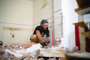 A man is installing tiles on a bathroom wall during a Bathroom Remodel.