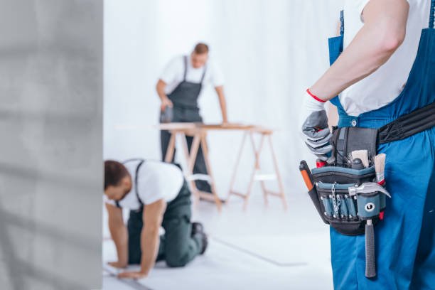 A man in overalls stands beside a wall filled with tools, representing Plainfield Remodeling Services.
